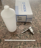 Photo of the Moen soap dispenser parts including the chrome pump, white refill bottle, and straw tube, all placed on a countertop next to the original box.