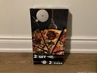 Box front showing pizza cutter set packaging with pizza photo and product images.