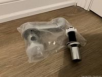 Two chrome plumbing parts still in plastic bag on floor: a P-trap and a drain assembly.