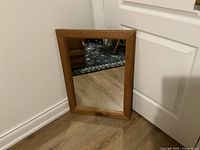 Front view of the rectangular pine wood framed mirror placed on floor next to a white door.