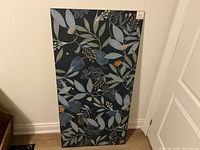 Front of large ceramic tile slab showing decorative floral pattern in blues, greens, and orange on black.