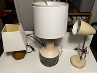 Three table lamps together showing different styles and sizes; one wood based with square shade, one large round base with cylindrical shade, one vintage metal with conical shade.