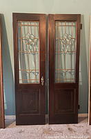 Front view of two tall dark stained wood doors with decorative leaded glass center panels and lower recessed panels