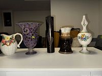 Seven vases in different shapes, sizes and styles displayed on a table against a neutral background, showing diversity of the collection.