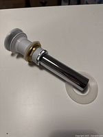 Photo showing Vigo vessel sink pop-up drain with chrome-finished pipe, brass tone nut, and white mounting ring on white surface.