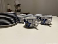 Photo of vintage cups and saucers arranged on a table, showing multiple larger and smaller cups with blue and yellow floral detailing.