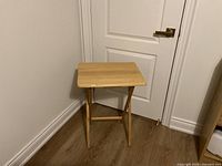 Wooden fold-up table standing upright in front of a white door on wooden floor.