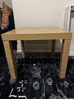 Front view of the solid wooden side table on a dark rug against a wall with pillows behind.