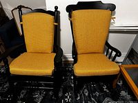 Front view of two black painted wooden rocking chairs with vibrant yellow seat and back cushions, showing style and cushion coverage.
