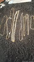 Seven different gold tone chains laid out on black background showing variety in styles and sizes