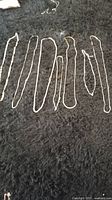 Seven silver tone chains laid out on black fabric background, showing various chain styles and lengths.