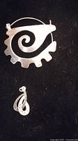 Two silver pendants on black background, one large signed M2 with spiral gear design, one smaller signed Taxco teardrop shaped pendant