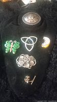 Five brooches displayed on black velvet, showing varying designs including floral, butterfly, Celtic knot, and crescent moon.