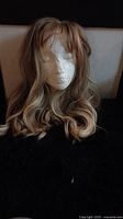 First image showing long wavy dark blonde wig with light blonde highlights and bangs on mannequin head.