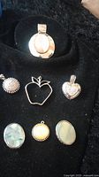 Vintage pendants including mother of pearl ovals, silver fruit shapes, rhinestone heart, yellow stone medallion, and silver sun with rhinestones shown on black velvet