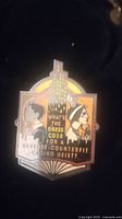 Close-up of enamel pin showing two characters, city buildings, and text.