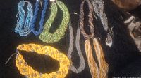 Seven multi-strand beaded necklaces arranged on black fabric, showing variety of colors and styles including twisted and braided strands.