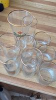 Clear glass set with gold rims including Carlsberg logo tall glass and six smaller glasses arranged on wood surface.