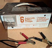 6 Amp Automatic Battery Charger with attached alligator clips shown on outdoor ground.