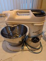 Vintage cream Kenwood Chef stand mixer with stainless steel bowl and attachments on a table.