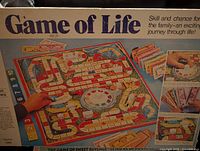 Photo of Game of Life board game showing colorful board with numbered spaces, money cards and spinner in center