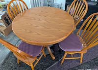 Round wooden kitchen table with four wooden spindle back chairs, purple cushions, placed on a dark rug.