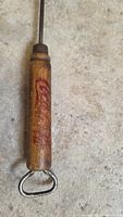 Close-up of wooden handle with faded red Coca Cola logo and metal bottle opener on floor background.