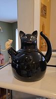Front view of black enamel cat-shaped kettle with mouse whistle on spout and curved tail
