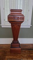 Full front view of antique mahogany plant stand showing tapering pedestal body, carved decorative panels, and removable black top.