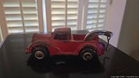 Side view of the red metal tow truck toy showing the tow arm and wheels.