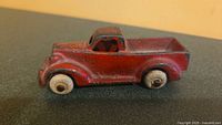 Side view of red 1930s Arcade cast iron truck with original white rubber tires, showing paint wear and detailed body shape.