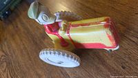 Photo showing side view of Donald Duck sitting on a red and yellow friction tractor with visible wear and original paint.