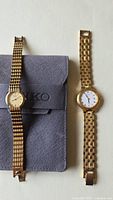 Two gold tone ladies watches shown side by side with a grey Seiko pouch beneath one watch.