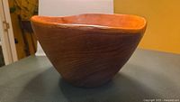 Side profile showing the teak wood grain and wave edge design of the bowl.