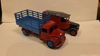 Photo showing two Dinky toy trucks, red and blue stake bed truck in front and a black and red truck behind.