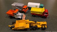 Five miniature Lesney trucks including dump trucks, delivery truck, and construction vehicle, shown from an angled top view.