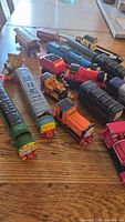 Group photo of 17 Thomas the Tank Engine themed trains and cars on a wood surface, showing varying colors and conditions.