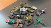 Wide shot of all 18 army toy vehicles including tanks, ambulances, motorcycles with sidecars, and airplanes on tabletop surface.