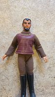 Front full body photo of vintage Star Trek Klingon figure showing brown padded vest, brown fabric pants, and black boots, worn condition.