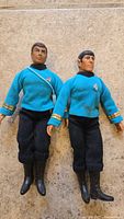 Full view of both vintage Star Trek figures, Spock on the right with black mark on shirt, and Dr. McCoy on the left in blue uniforms and black pants.
