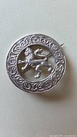 Front view of circular silver brooch pin with lion design and Celtic knot border