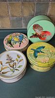 Four vintage round metal cookie tins with painted bird and floral designs on lids