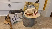 Lot of fishing-themed items including fishing hat, wooden gear, poster, bucket, and box.