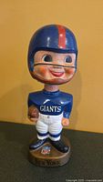 Front view of the vintage ceramic football player nodder showing NY Giants blue helmet, jersey, holding football, and base with NFL logo and New York text.