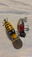 Two vintage Heddon fishing lures showing distinct color patterns and hooks.