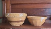 Two vintage stoneware mixing bowls side by side, large on left with brown stripes and embossed pattern, smaller plain on right