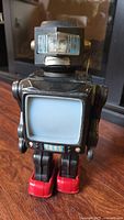 Full view of black vintage tin robot toy standing approximately 12 inches tall with red boots and lighted screen torso, head showing human face graphic.
