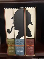 Three hardcover volumes of The New Annotated Sherlock Holmes with silhouette dust jackets showing different Holmes profiles and spines in green, blue, and maroon.