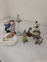 Overview of nine porcelain figurines including teacup and saucer set with mice, Mr. Toad and female frog, dwarf, Jiminy Cricket, Siamese cats, Donald Duck, bird in cage.