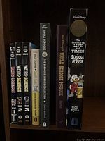 Spines of seven hardcover graphic novels on shelf: Weird Science Vol. 1–3 and four Uncle Scrooge McDuck collections